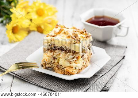 A Piece Of Homemade Kyiv Cake Or Dacquoise Cake On The White Plate With Cup Of Tea And Flowers On Th