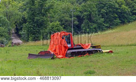 Snow Groomer Under Tarp Parked At Grass Field During Summer