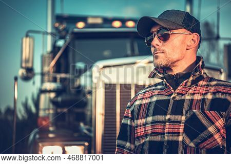 Proud Semi Truck Driver Portrait In Front Of The Vehicle. Caucasian Trucker In His 40s Wearing Baseb