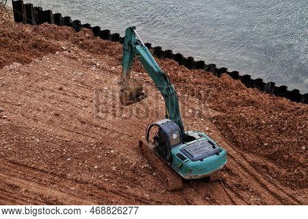 Green Excavator Flatten The Ground Near The Water Or The River.