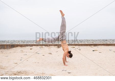 Shirtless Caucasian Man Doing Backflip On Pebble Beach.