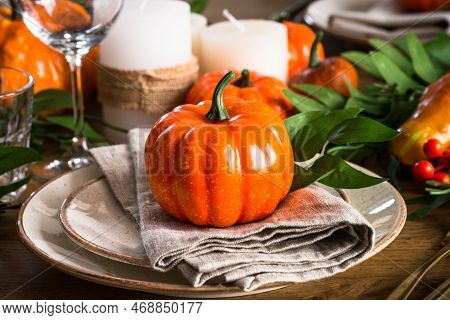 Autumn Table Setting With Plate, Pumpkin And Candles At Wooden Table. Thanksgiving Food Festive Dinn