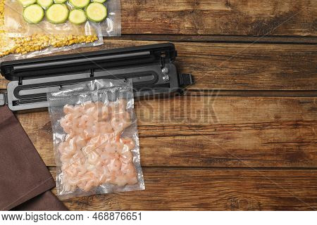Vacuum Packing Sealer And Plastic Bags Of Different Food On Wooden Table, Flat Lay. Space For Text