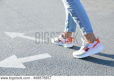 Choice Of Way. Woman Walking To Drawn Mark On Road, Closeup. White Arrows Pointing In Different Dire