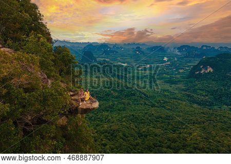 Dragon Crest Mountain Krabi Thailand, A Young Traveler Sits On A Rock That Overhangs Abyss At Sunset