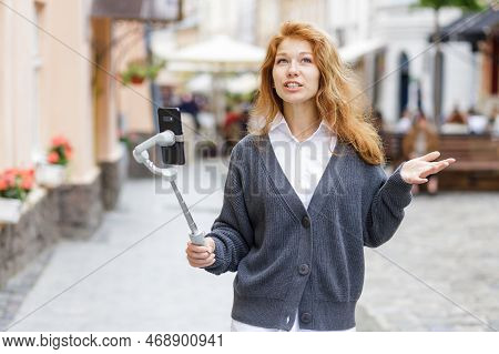 Young Redheaded Beautiful Woman Walking And Using Her Mobile Phone