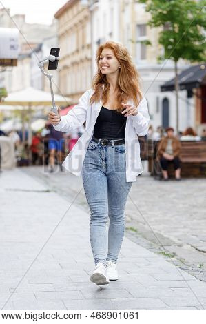 Young Redheaded Beautiful Woman Walking And Using Her Mobile Phone