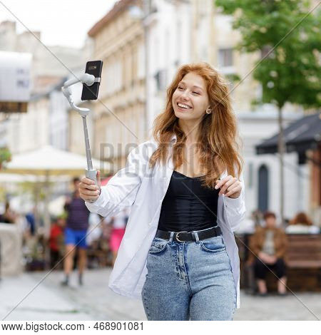 Young Redheaded Beautiful Woman Walking And Using Her Mobile Phone