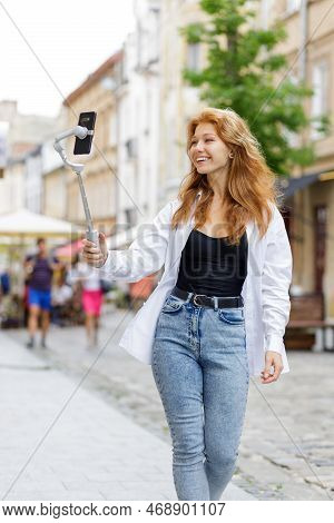 Young Redheaded Beautiful Woman Walking And Using Her Mobile Phone