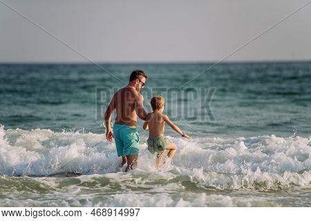 Father With His Little Son Entering In To Ocen, Enjoying Summer Vacation.