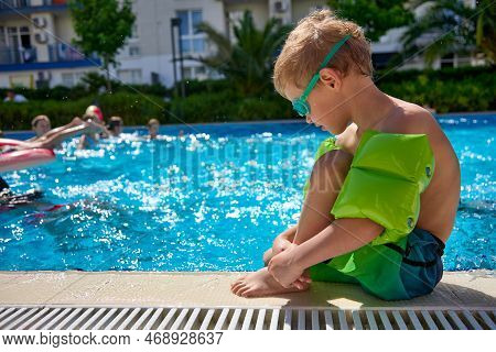 Sad Boy In Bathing Shorts Sits Near The Outdoor Pool In Summer, They Are Not Allowed To Swim. Small 