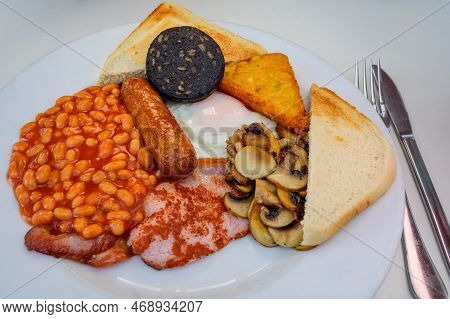 White Board With Full English Breakfast With Bacon, Fried Egg, Beans, Tomato, Roasted Sausage, Black