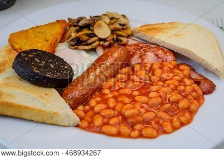 White Board With Full English Breakfast With Bacon, Fried Egg, Beans, Tomato, Roasted Sausage, Black