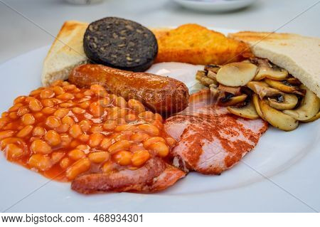 White Board With Full English Breakfast With Bacon, Fried Egg, Beans, Tomato, Roasted Sausage, Black