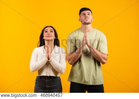 Serious Concentrated Millennial Arab Husband And Wife Folded Hands In Supplication, Make Wish, Pray