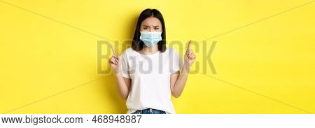 Covid-19, Pandemic And Social Distancing Concept. Disappointed Asian Girl In Medical Mask, Frowning 