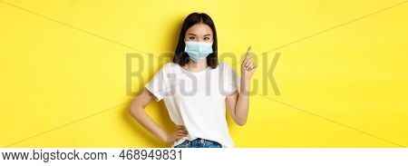 Covid, Health Care And Pandemic Concept. Asian Female Model In Medical Mask And White T-shirt Pointi