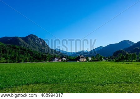 Panoramic View Of Beautiful Mountain Landscape, Green Austrian Village In The Alps, Mountains Surrou