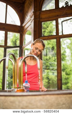 Young woman fillig a plastic bottle with healthy mineral water from a wellspring in a spa (shallow DOF)