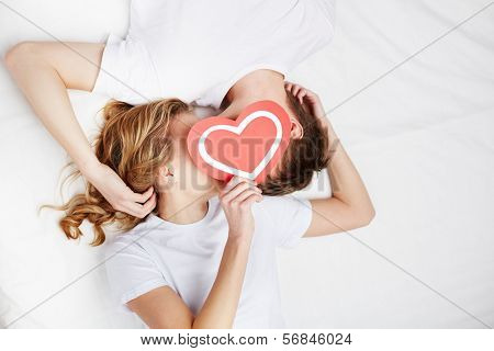Two young dates behind paper heart with their faces close to one another