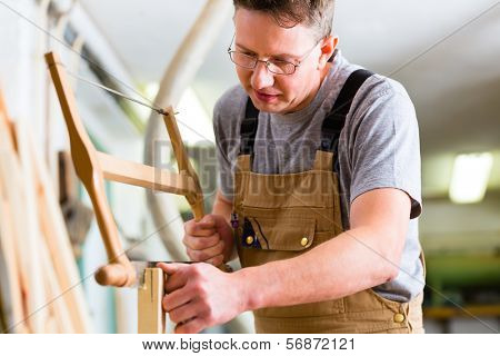 Carpenter working on a hand saw cutting a tenon in drawers in his workshop with bow or frame saw