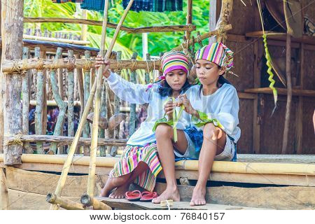two young beautiful child girls in traditional clothes in bamboo house making toys from palm leaves, Philippines, Malay, Panay