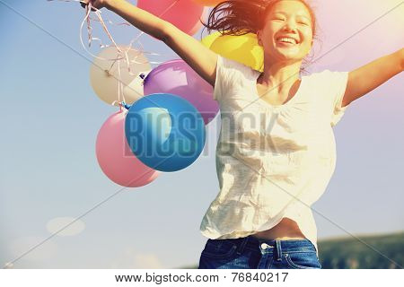 young asian woman jumping on green grassland with colored balloons