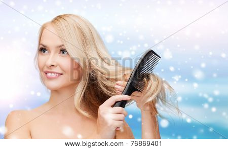 heath, people, haircare and beauty concept - beautiful young woman with bare shoulders combing her hair over blue sky, snow and clouds background