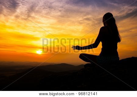 Yoga practicioner sitting on rock during the sunset meditation