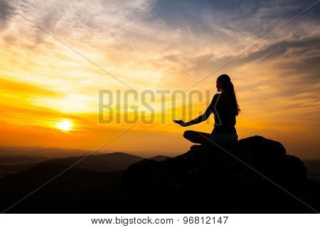 Yoga practicioner sitting on rock during the sunset meditation