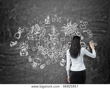 Brunette Woman Is Drawing Shopping Icons On The Chalk Board.