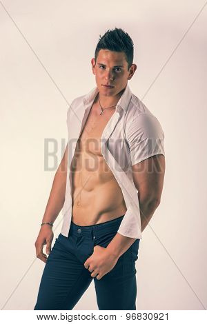 Young man displaying his muscular torso holding open his stylish shirt