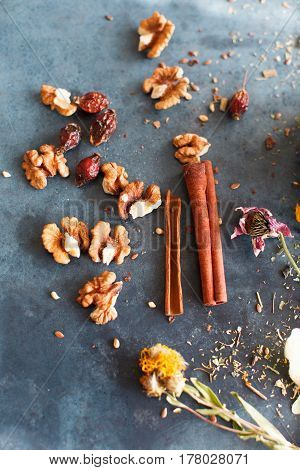 Cinnamon sticks nuts and a herb collection scattered on a blue table a glass jar with tea lime mint lemon balm chamomile. Daylight vertical image.