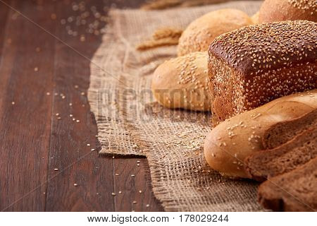 Different bread on burlap on the wooden table close-up. With wheat and ears of wheat. Slices of the brown bread. Rulls and baguette.
