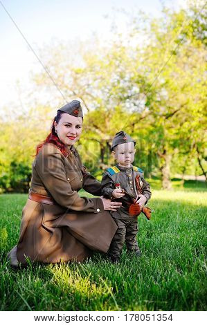 A small son with his mother in the uniform of a Soviet soldier against the background of nature. May 9, Victory Day, World War II, family, peace, against fascism.