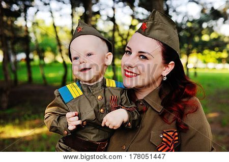 A small son with his mother in the uniform of a Soviet soldier against the background of nature. May 9, Victory Day, World War II, family, peace, against fascism.
