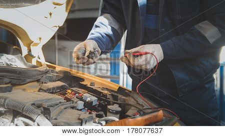 Mechanic in auto workshop works with car electrics - electrical wiring, voltmeter, close up