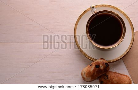 On a wooden table on the right is a demitasse with a gold rim. Near the coffee cup is homemade shortbread with chocolate.