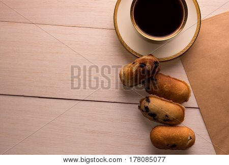 On a wooden table on the right is a demitasse with a gold rim. Near the coffee cup are four homemade cookies with chocolate.