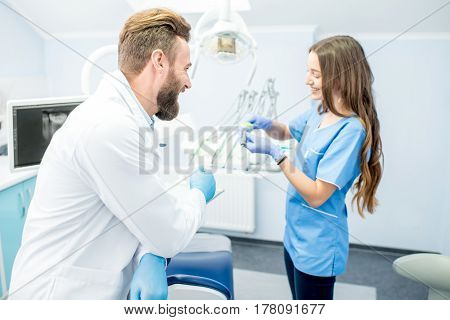 Handsome dentist with young female assistant in uniform prepairing for the job at the dental office