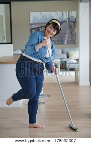 Cheerful overweigth woman having fun sweeping the floor