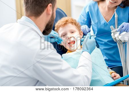 Children's dentist examinating baby teeth of a young boy sitting on the dental chair at the office