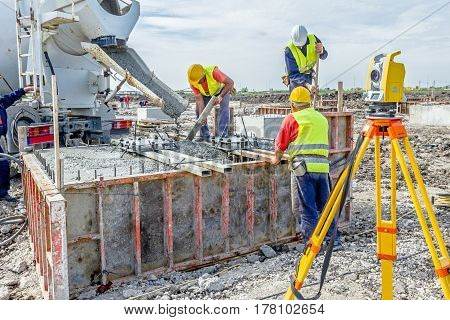 Workers at building site are pouring concrete in mold from mixer truck.