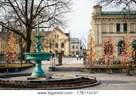 UPPSALA SWEDEN - Mar 26 2016 - Street view of inactive fountain with traditional colourful feathers on trees for Easter decorations in Uppsala Sweden Europe