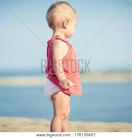 Baby playing on the sandy beach near the sea. Cute little girl in red dress with sand on tropical beach. Ocean coast.