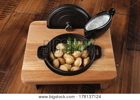 Cooked meat dumplings (pelmeni, chuchpara) in black pan with sauce. wooden background.