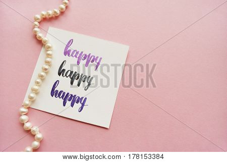 Happy handwritten with watercolor in calligraphy style. Composition on a pink background. Top view.