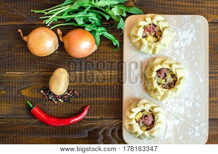 A national Uzbek dish - balish with meat onion red pepper potatoes and herbs in the form of a smile on a brown wooden table