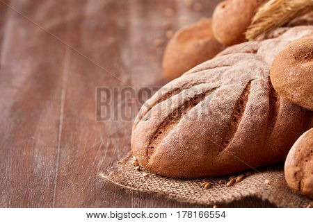 handmade tasty bread lying on burlap on the wooden table with flour, wheat and ears of wheat. Brown bread and rulls. Delicious food. Fresh baking. Tasty and appetizing.
