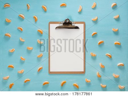 Blank clipboard on pastel blue color table with citrus tangerine slices, minimal style, flat lay.